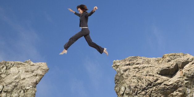 Mixed race businesswoman jumping over gap between cliffs