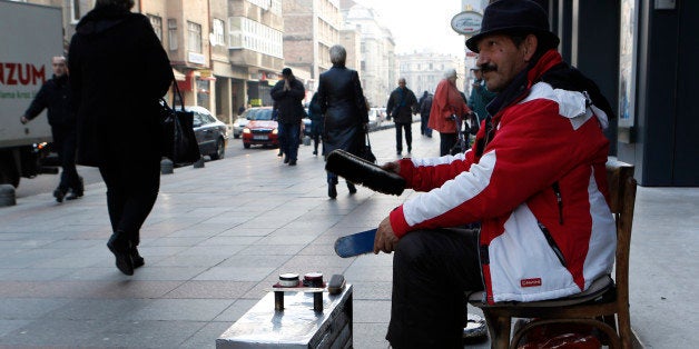 In this Friday, Dec. 19, 2014, photo shoe shiner Ramiz Hasani waits for customers on the main street in Sarajevo, Bosnia. Ra