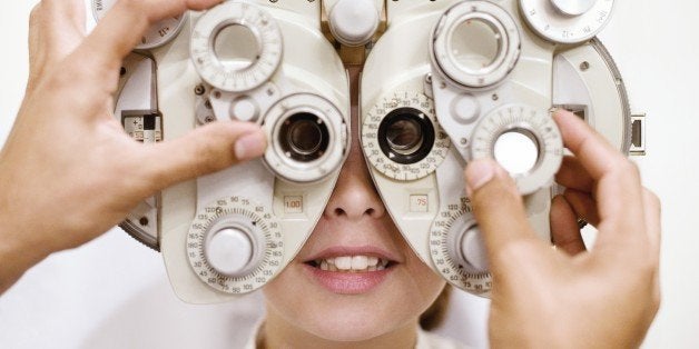 Eye examination. Optician using a phoropter to examine a ten year old girl's eyes. This device is used to measure the refract