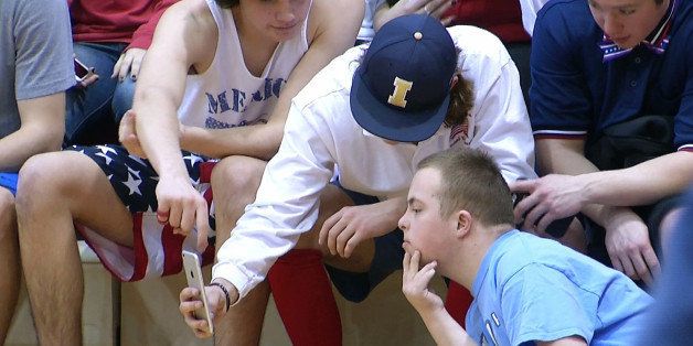 In this Friday, Feb. 13, 2015 image made from video, Independence High School seniors Jake Current, wearing baseball cap, and Daniel Wood, lower right, look at a smartphone during a high school basketball game in Brentwood, Tenn. In an act of kindness, the Independence High basketball team crowned Wood, a student born with Down Syndrome, Coming Home King, which is usually reserved for the most popular students. (AP Photo/Alex Sanz)