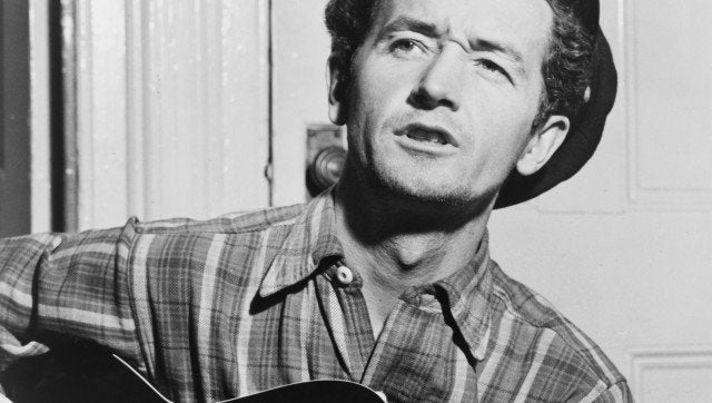 Description Woody Guthrie, half-length portrait, facing slightly left, holding guitar / World Telegram photo by Al Aumuller.