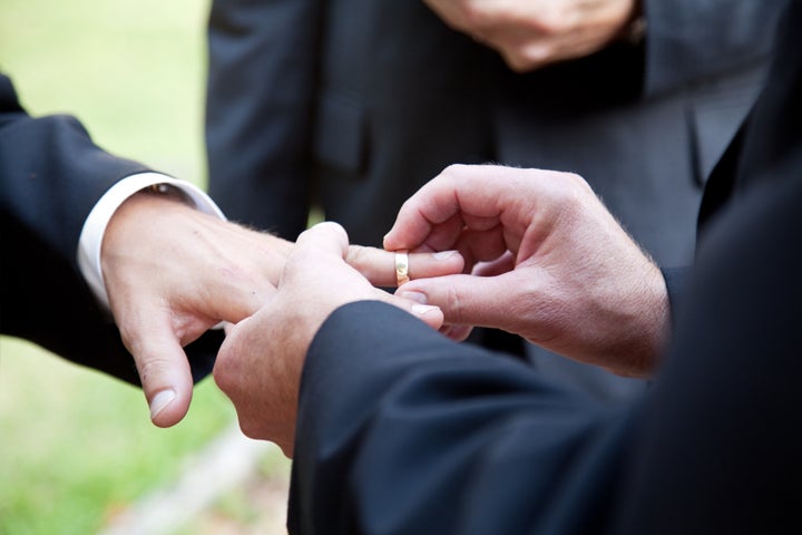 one groom placing the ring on...