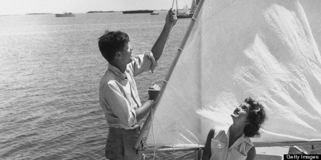 1955: American politician John F Kennedy (1917 - 1963) stands at the water's edge hoisting the sail of a small boat, upon which kneels his wife, Jacqueline Bouvier Kennedy (1929 - 1994), Hyannis Port, Massachusetts. (Photo by Hulton Archive/Getty Images)