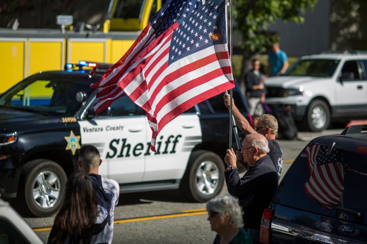 A man waves a flag in Thousand Oaks, California, as a Ventura County Sheriff's patrol car passes. Deputies visited the suspected gunman's home in April.