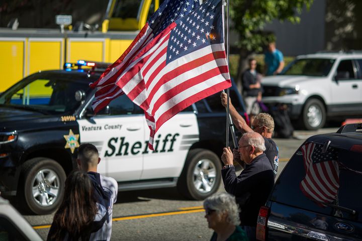 A man waves a flag in Thousand Oaks, California, as a Ventura County Sheriff's patrol car passes. Deputies visited the suspected gunman's home in April.