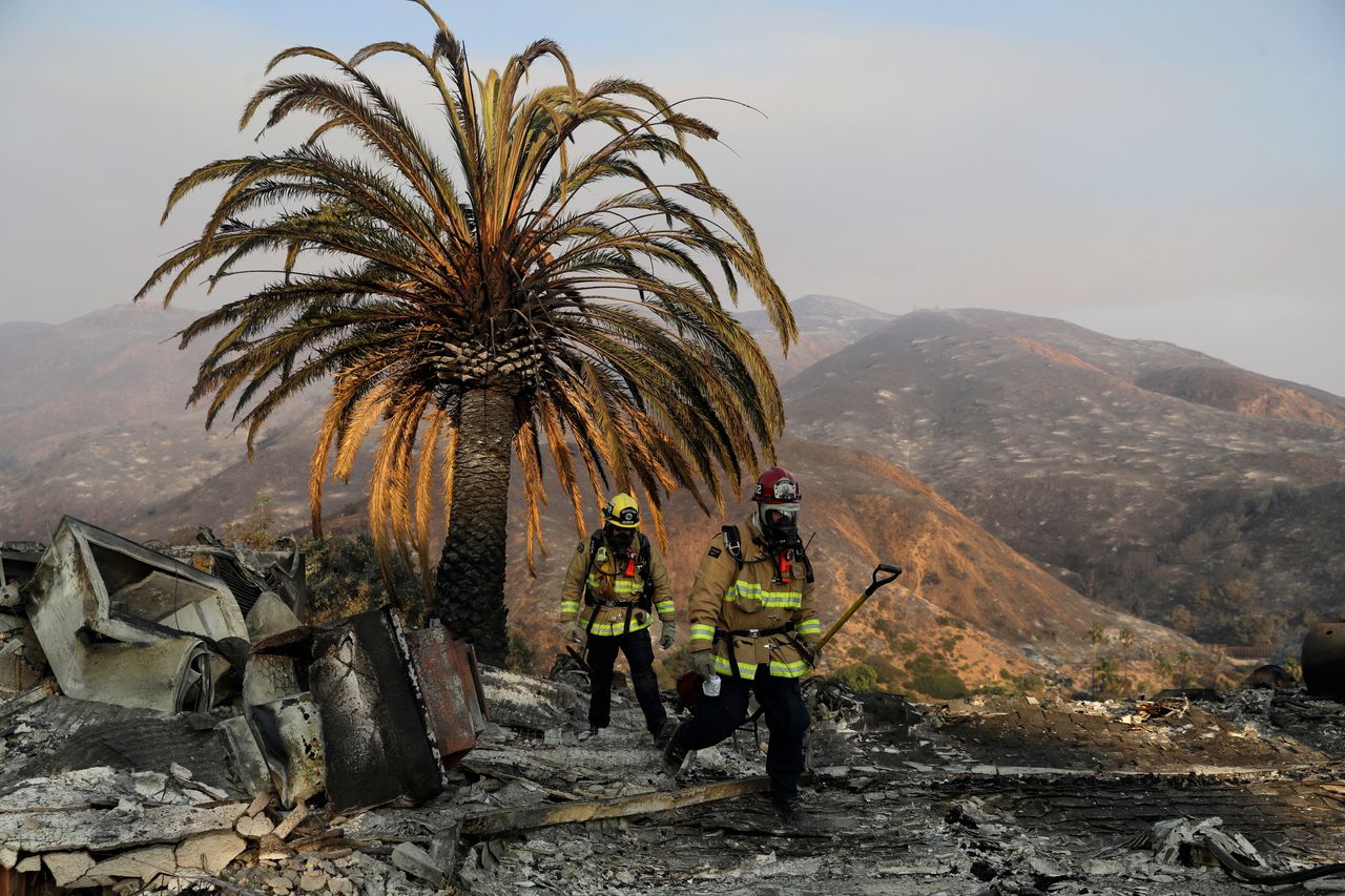Firefighters Jason Toole, right, and Brent McGill with the Santa Barbara Fire Dept. walk among the ashes of a wildfire-ravaged home after turning off an open gas line on the property in Malibu, Calif.