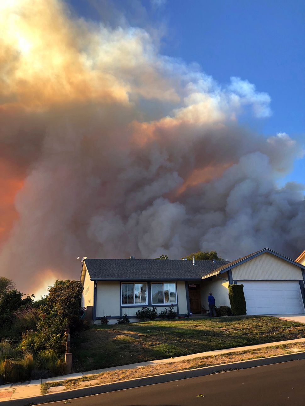 Plumes of smoke loom in the sky several miles away, seen behind a home in Thousand Oaks, Calif.
