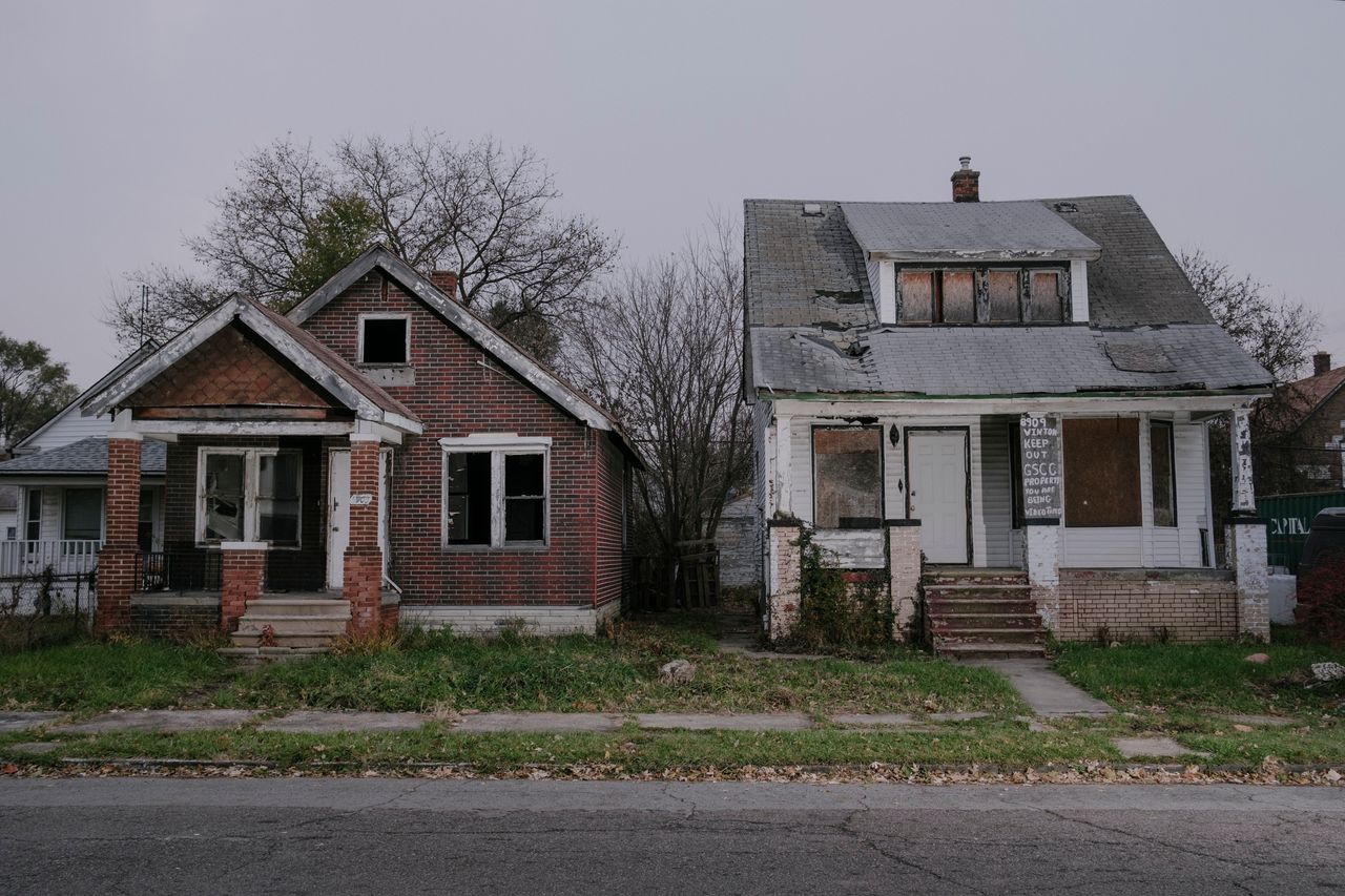 At left, a house owned by the Detroit Land Bank Authority and, at right, a vacant house owned by Covington and the Georgia Street Community Collective. The Land Bank required Covington to board up the house or possibly lose ownership, though the Land Bank has yet to board up this and other houses on the same block.