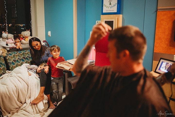Madi, with his mother and brother, watches his father prepare to cut his hair in solidarity.