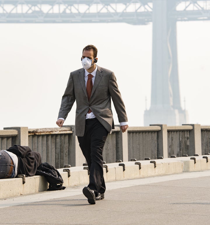 A man wears a mask while another person sleeps on the ground as smoke from the Camp Fire fills the air in San Francisco on Nov. 15, 2018.