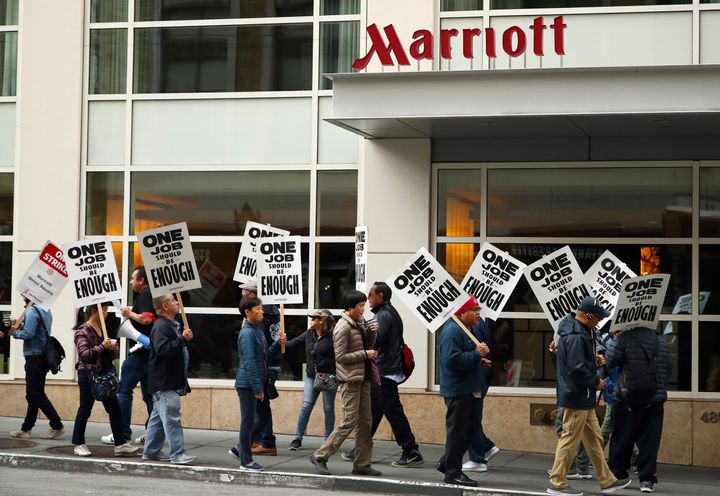 In this Oct. 4, 2018, photo, hotel workers carrying signs that say "One Job Should Be Enough" strike in front of a Marriott hotel in San Francisco.