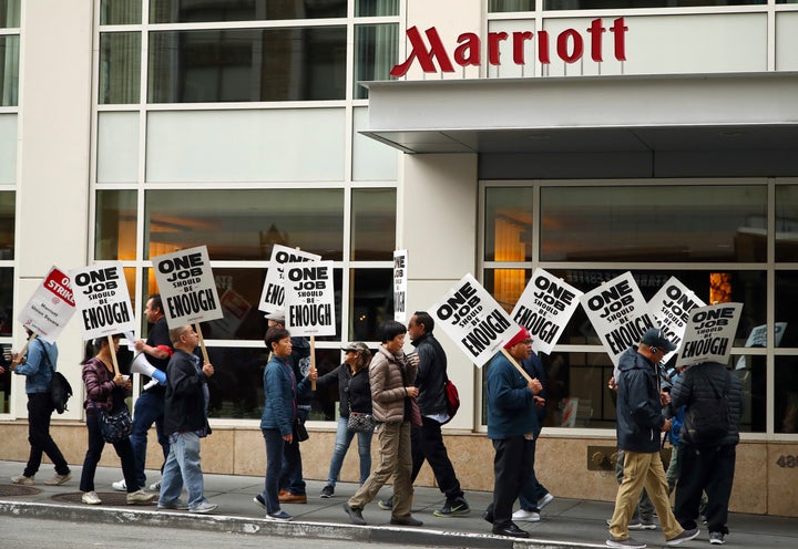 In this Oct. 4, 2018, photo, hotel workers carrying signs that say "One Job Should Be Enough" strike in front of a Marriott hotel in San Francisco.