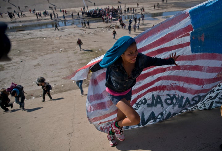 A migrant woman helps carry a handmade U.S. flag up the riverbank at the Mexico-U.S. border after getting past Mexican police