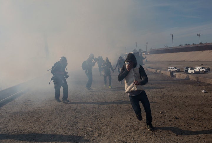 Migrants run from tear gas launched by U.S. agents, amid photojournalists covering the Mexico-U.S. border, after a group of m
