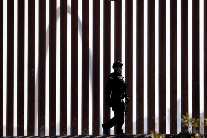 A U.S. Customs and Border Protection Special Response Team officer walks along a border wall, as the Monumental Arch in Tijua