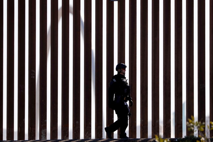 A U.S. Customs and Border Protection Special Response Team officer walks along a border wall, as the Monumental Arch in Tijuana, Mexico, sits behind, Sunday, Nov. 25, 2018, in San Diego. Migrants approaching the U.S. border from Mexico were enveloped with tear gas Sunday after a few tried to breach the fence separating the two countries. (AP Photo/Gregory Bull)