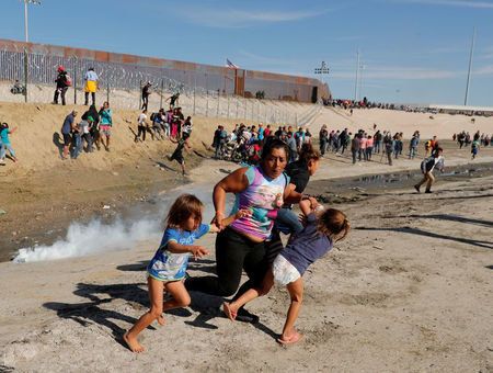 Maria Meza, a 40-year-old woman from Honduras traveling as part of a caravan of thousands from Central America to the United States, runs away from tear gas with her 5-year-old twin daughters Saira Mejia Meza and Cheili Mejia Meza.