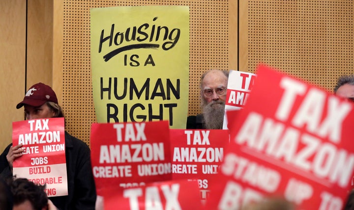 People hold signs at a Seattle City Council meeting on May 14, 2018, to advocate for a tax on large businesses like Amazon and Starbucks to fight homelessness.