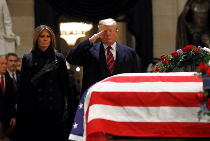 President Donald Trump salutes alongside first lady Melania Trump in front of the flag-draped casket of former President Geor