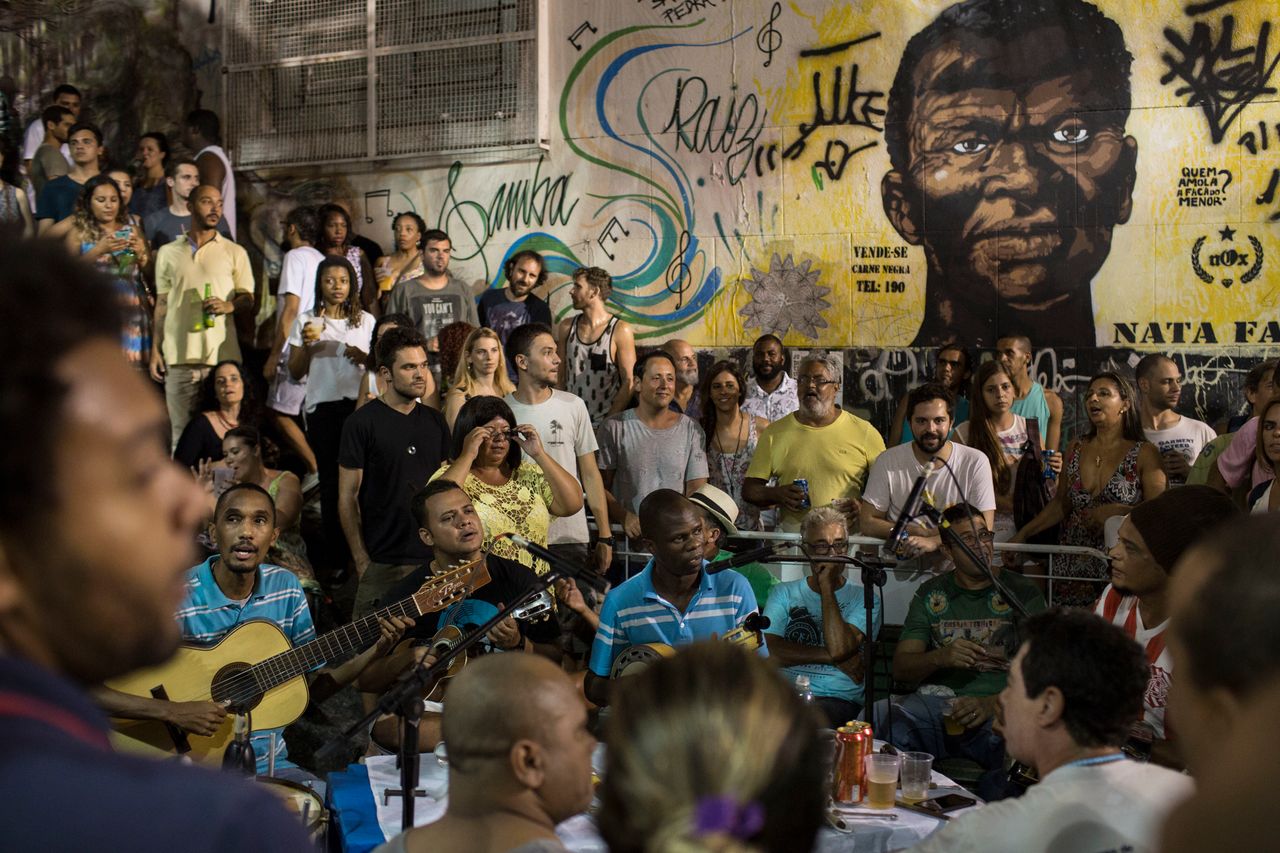 In this March 29, 2016 photo, people listen to live samba music at Pedra do Sal in Rio de Janeiro. A mural in the background features a portrait of Zumbi dos Palmares.