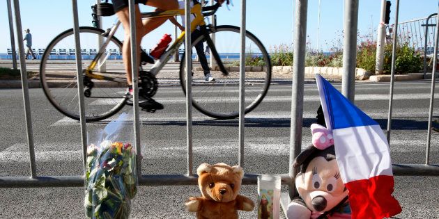 A man cycles past a bouquet of flowers, stuffed toys and a French flag placed in tribute to victims, two days after an attack by the driver of a heavy truck who ran into a crowd on Bastille Day killing scores and injuring as many on the Promenade des Anglais, in Nice, France, July 16, 2016. REUTERS/Pascal Rossignol