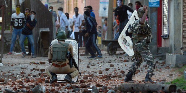 An Indian security offciers throws a stone to Kashmiri protestors during a clash in Batmaloo area of Srinagar on July 28, 2016.