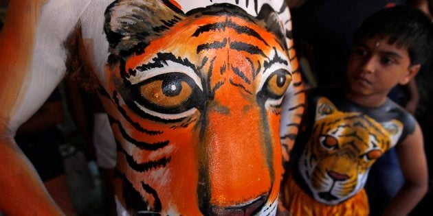 A child, his body painted in the likeness of a tiger, looks at the body art of an adult before performing the annual 'Pulikali' or Tiger Dance in Thrissur.