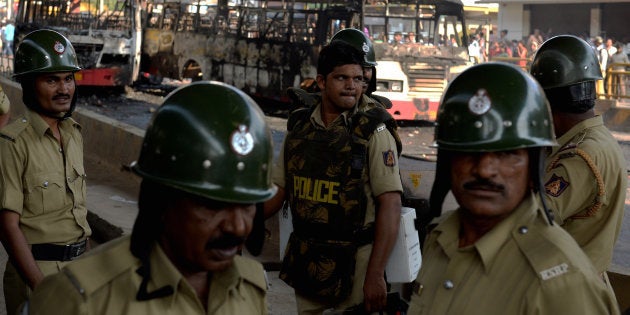 Police personnel stand guard near burnt buses after violence that followed a protest by garment factory workers in Bangalore.