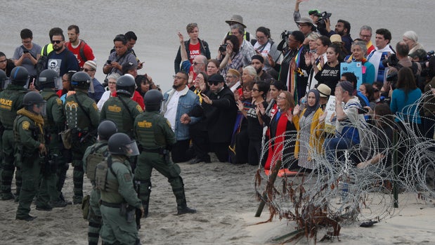 U.S. police and Border Patrol hold a line as members of an inter-faith group hold a prayer session to show support for Central American asylum-seekers who arrived in recent caravans and call for an end to detaining and deporting immigrants, in San Diego as seen from across the border wall in Tijuana, Mexico, Monday, Dec. 10, 2018. The Border Patrol arrested 31 protestors for trespassing as they tried to approach the border wall, and one person for assaulting an officer.(AP Photo/Rebecca Blackwell)