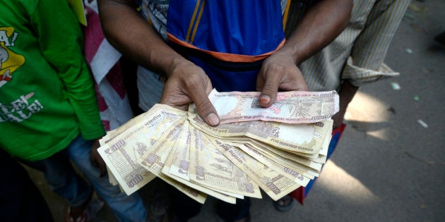 File photo of a man holding Rs. 500 and Rs. 1000 bank notes while waiting in line outside a bank to exchange them.