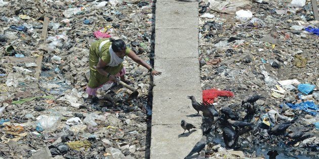 In this photograph taken on June 3, 2015, an Indian woman attempts to clean a clogged open sewage drain adjoining a slum in Mumbai in Mumbai.