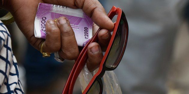 NEW DELHI, INDIA - NOVEMBER 13: A lady holds a 2000 rupee currency as she waits in a long queue to withdraw or deposit their old currency Rs. 500 and 1000 outside a bank at Connaught Place, on November 13, 2016 in New Delhi, India. Tempers frayed as hundreds of thousands of people queued for hours outside banks to swap 500 and 1,000 rupee bank notes after the notes were abolished earlier in the week. Nearly half of India's 2,02,000 ATMs were shut on Friday and those that operated quickly ran out of the new notes as scores of people descended upon them. (Photo by Vipin Kumar/Hindustan Times via Getty Images)