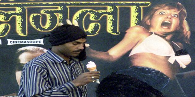 An Indian man passes a wall of a cinema displaying a poster of an adult movie in New Delhi.