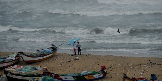 Residents walk near boats as waves break on the cost of the Bay of Bengal in Chennai.