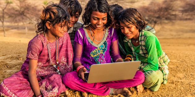 Happy Indian children, sitting on a sand dune and using laptop in desert village, Thar Desert, Rajasthan, India.