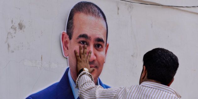 An Indian supporters of the Congress Party keeps his hand on the face of a cut out of billionaire jeweler Nirav Modi during a protest in New Delhi on February 16, 2018.