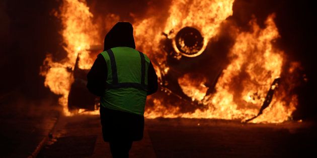 A demonstrator watches a burning car near the Champs-Elysees avenue during a demonstration Saturday, Dec.1, 2018 in Paris. French authorities have deployed thousands of police on Paris' Champs-Elysees avenue to try to contain protests by people angry over rising taxes and Emmanuel Macron's presidency.