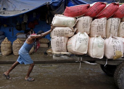 A labourer pushes a handcart loaded with sacks containing tea packets, towards a supply truck at a wholesale market in Kolkata.