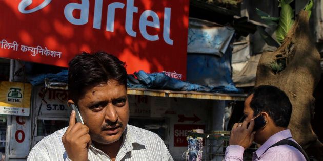 Pedestrians talk on their mobile phones in front of a store displaying a Bharti Airtel Ltd. advertisement in Mumbai, India, on Wednesday, Jan 29, 2014. The auction of wireless spectrum permits in India is scheduled for Feb. 3. Photographer: Dhiraj Singh/Bloomberg via Getty Images