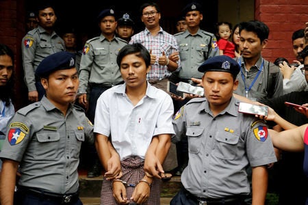 Reuters reporters Wa Lone and Kyaw Soe Oo, shown handcuffed in the center above, have been imprisoned for more than a year no