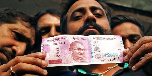 A man displays a new 2000 Indian rupee banknote after withdrawing from a bank.