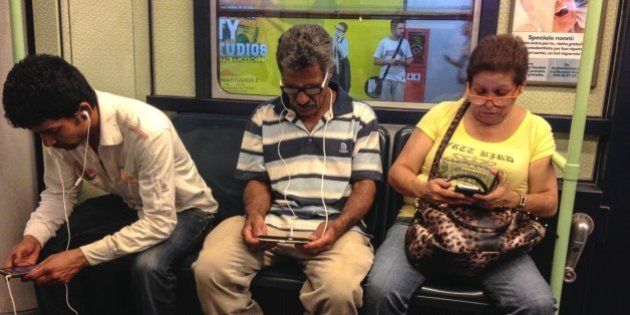 Three commuters comfortably Seated in the subway train Busy working on their electronic device. Milano, Italy