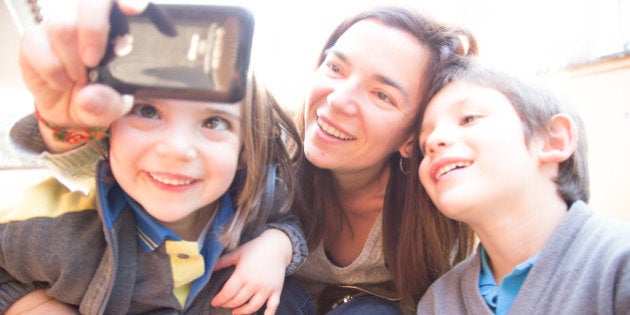 Mother with kids taking photos with smartphone in funny moment and sunset light.