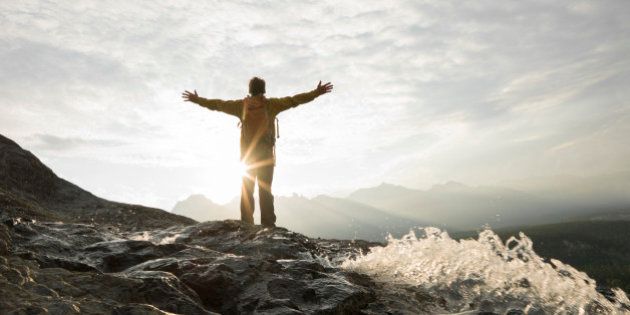 Man raises arms to sunrise over mountains, water