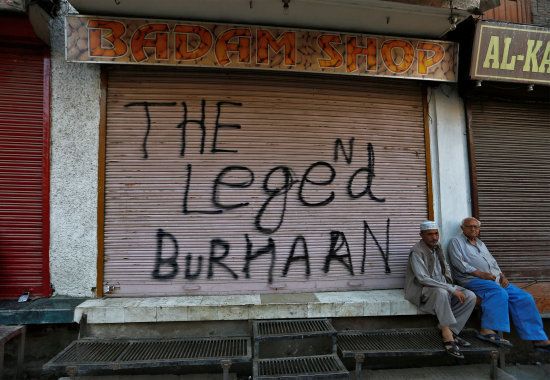 Men sit in front of a closed shop painted with a graffiti during a curfew in Srinagar July 12, 2016. REUTERS/Danish Ismail
