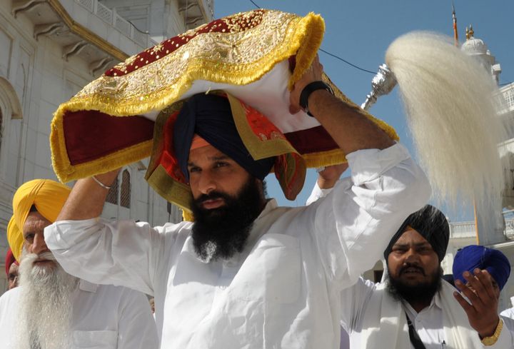 Indian Punjab Revenue Minister Bikram Singh Majithia (C) carries the Guru Granth Sahib following a religious punishment for altering a Sikh hymn to include the name of BJP candidate for Amritsar in India's general election Arun Jaitley at the Golden Temple in Amritsar on May 14, 2014.