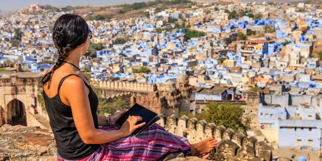 Young female tourist using digital tablet. The blue city of Jodhpur on the background. Jodhpur is known as the Blue City due to the vivid blue-painted houses around the Mehrangarh Fort.