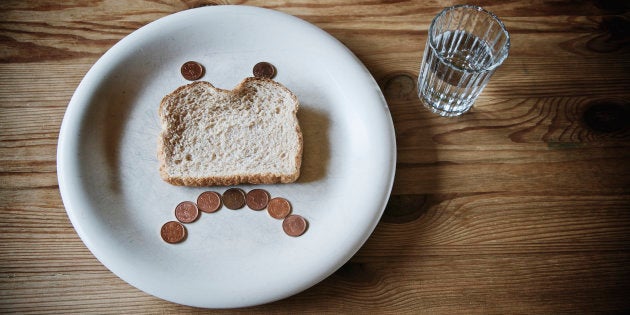 Glass of water and sad face made out of a slice of stale bread and pennies on a white plate