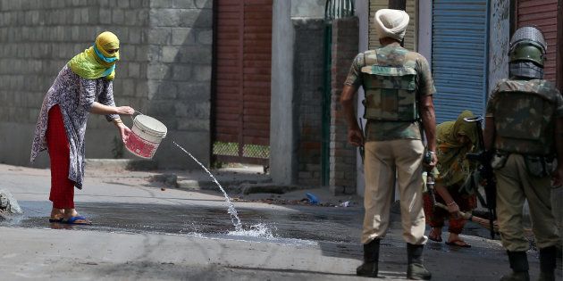 Women wash the street outside their house in Srinagar as security forces patrol during a curfew following weeks of violence in Kashmir August 19, 2016.