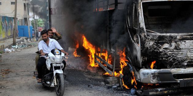 Men ride a motorcycle past a lorry in Bengaluru, which was set on fire by protesters, India September 12, 2016.